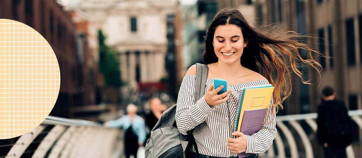 Student walking with folders and books smiling at her phone